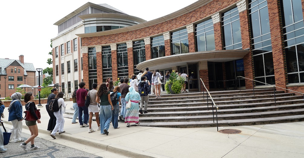 Diverse group of prospective students and families walking up steps and gathering outside modern brick University of Michigan School of Public Health building during campus visit or admissions event