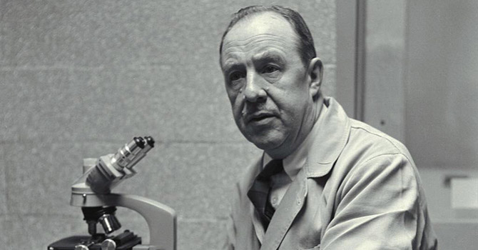 Black and white photo of Thomas Francis sitting next to a microscope in a laboratory.