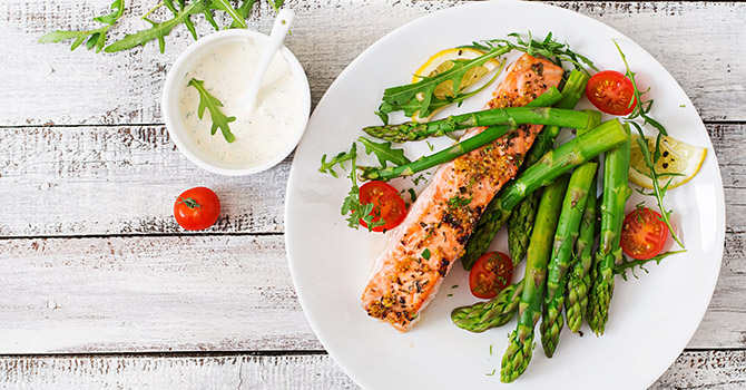 A plate of salmon and asparagus on a white wood table.