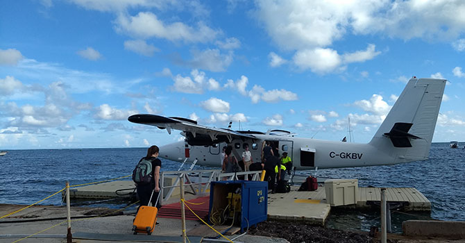 Students walking with luggage to a small airplane by the water.