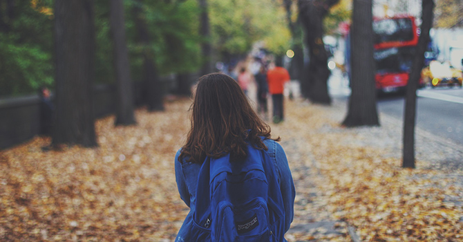 Child with a backpack walking down a paved sidewalk.