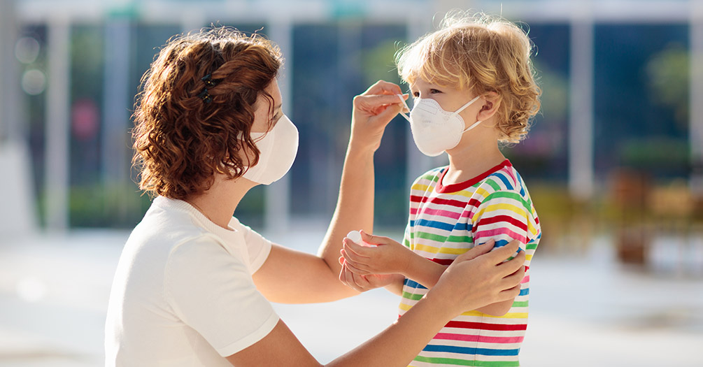 A woman helping to put a mask on a young child.