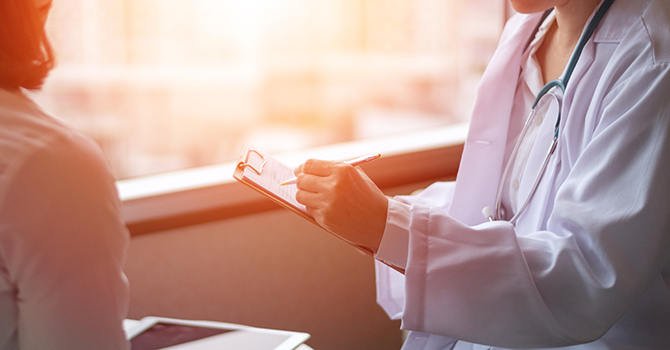 Doctor holding a clipboard talking to a patient.