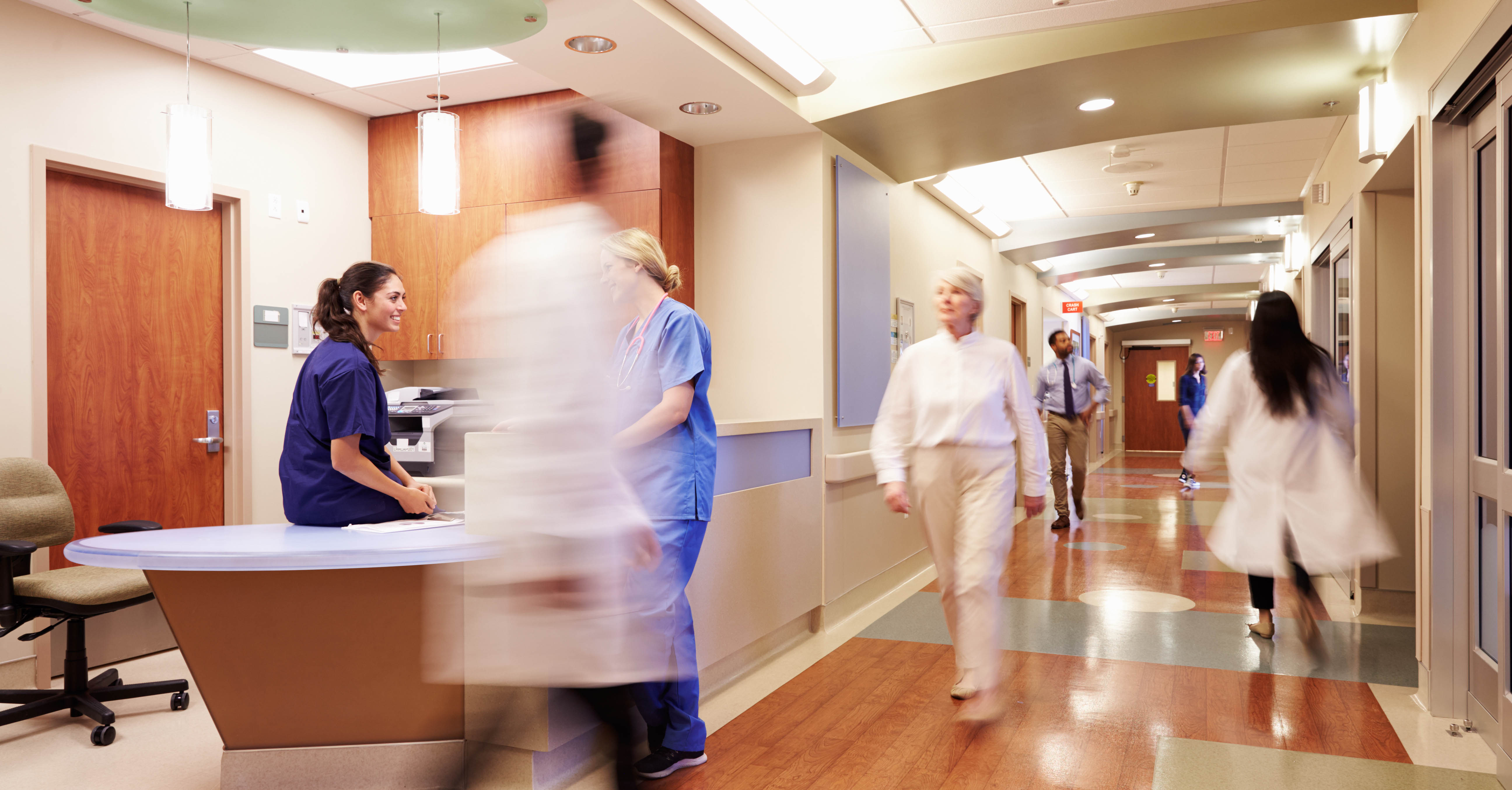 People walking past the nurse's station in a hospital.