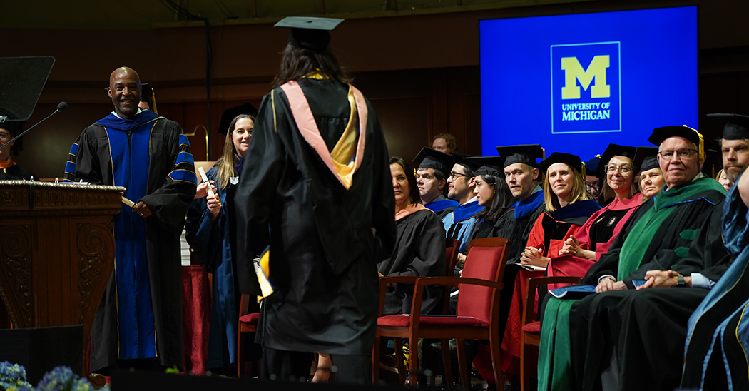 Dean F. DuBois Bowman, far left, greats a Class of 2025 graduate on stage as the Michigan Public Health faculty look on.