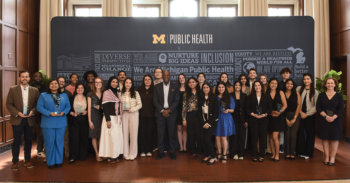 A crowd shot of the dean of the School of Public Health and the award winners in front of a Michigan Public Health banner