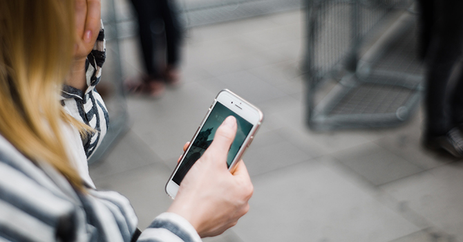 Woman in black and white striped shirt holding an iPhone.