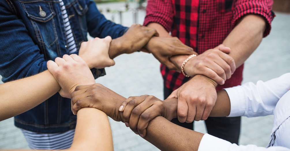 Image of a diverse group of people holding wrist in a circle
