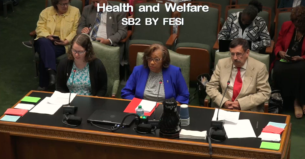A photograph of three people sitting at a desk, testifying before a governmental committee